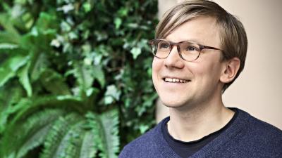 Henkilö Tuomo Rainio hymyilee, taustalla viherseinä