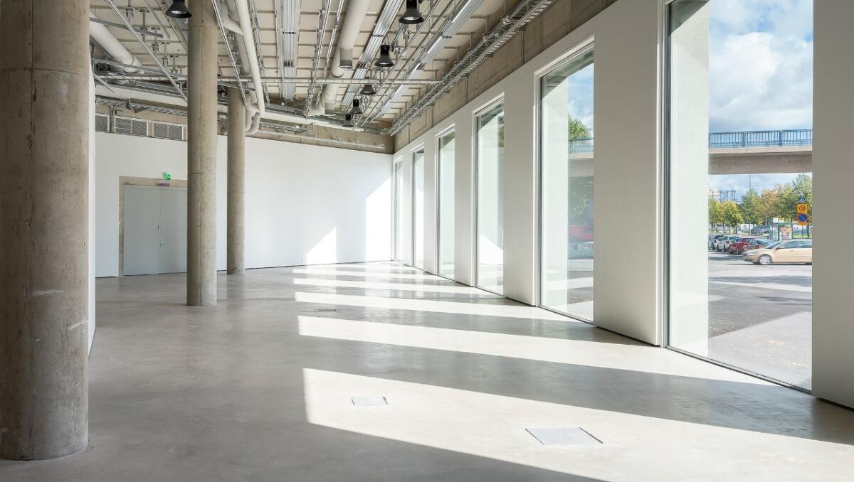 Tyhjä, valoisa galleriatila suurilla ikkunoilla.