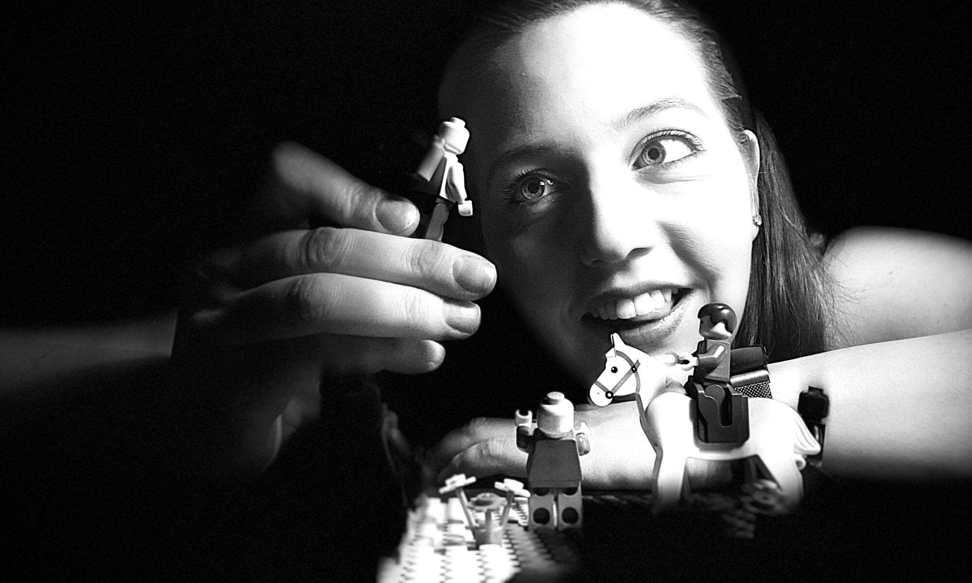 A young woman plays with lego figurines in a black and white picture