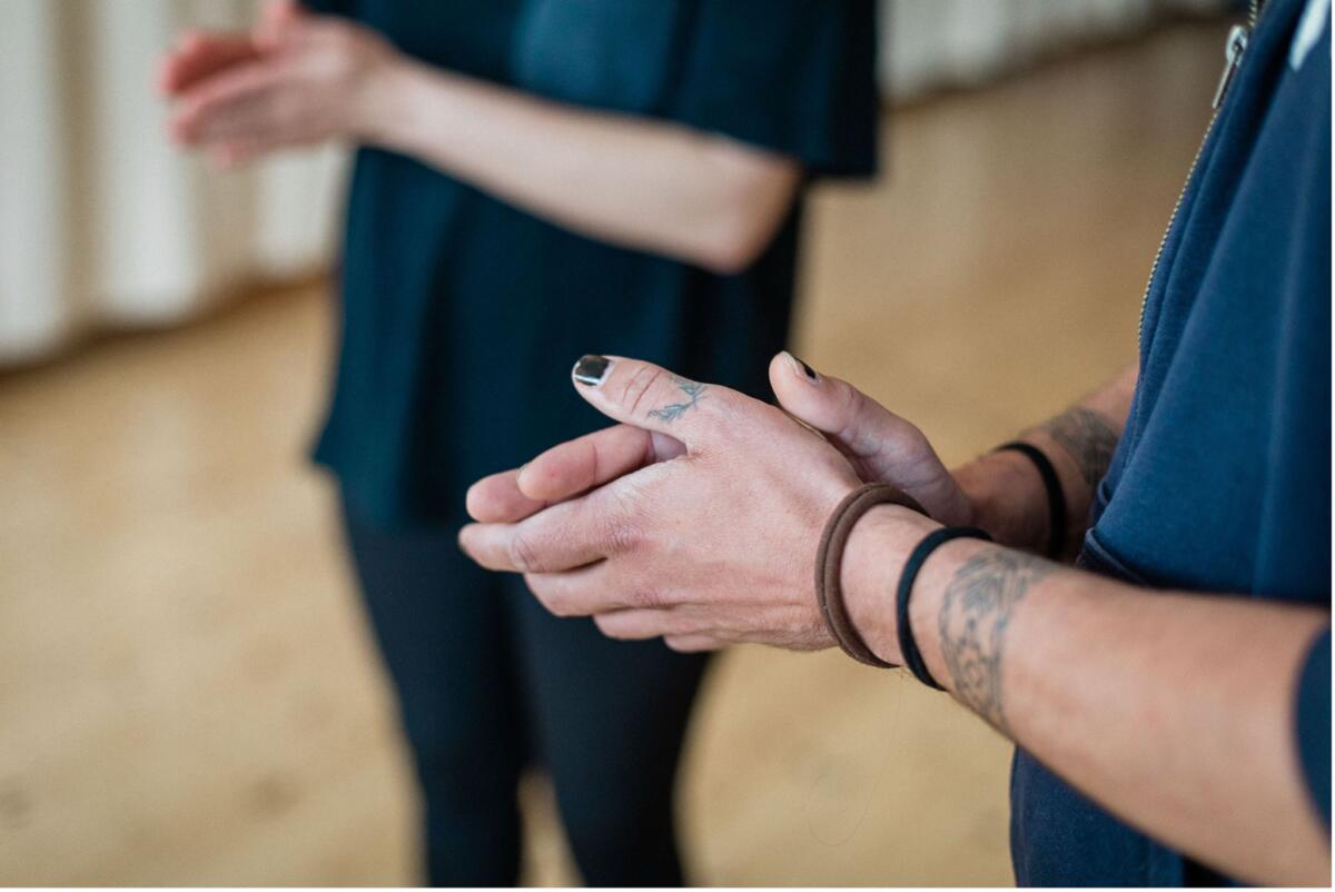 Two white people stand hands together in a room with a wooden floor.