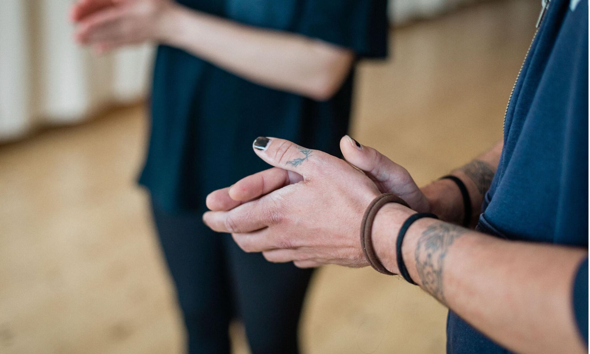 Two white people stand hands together in a room with a wooden floor.