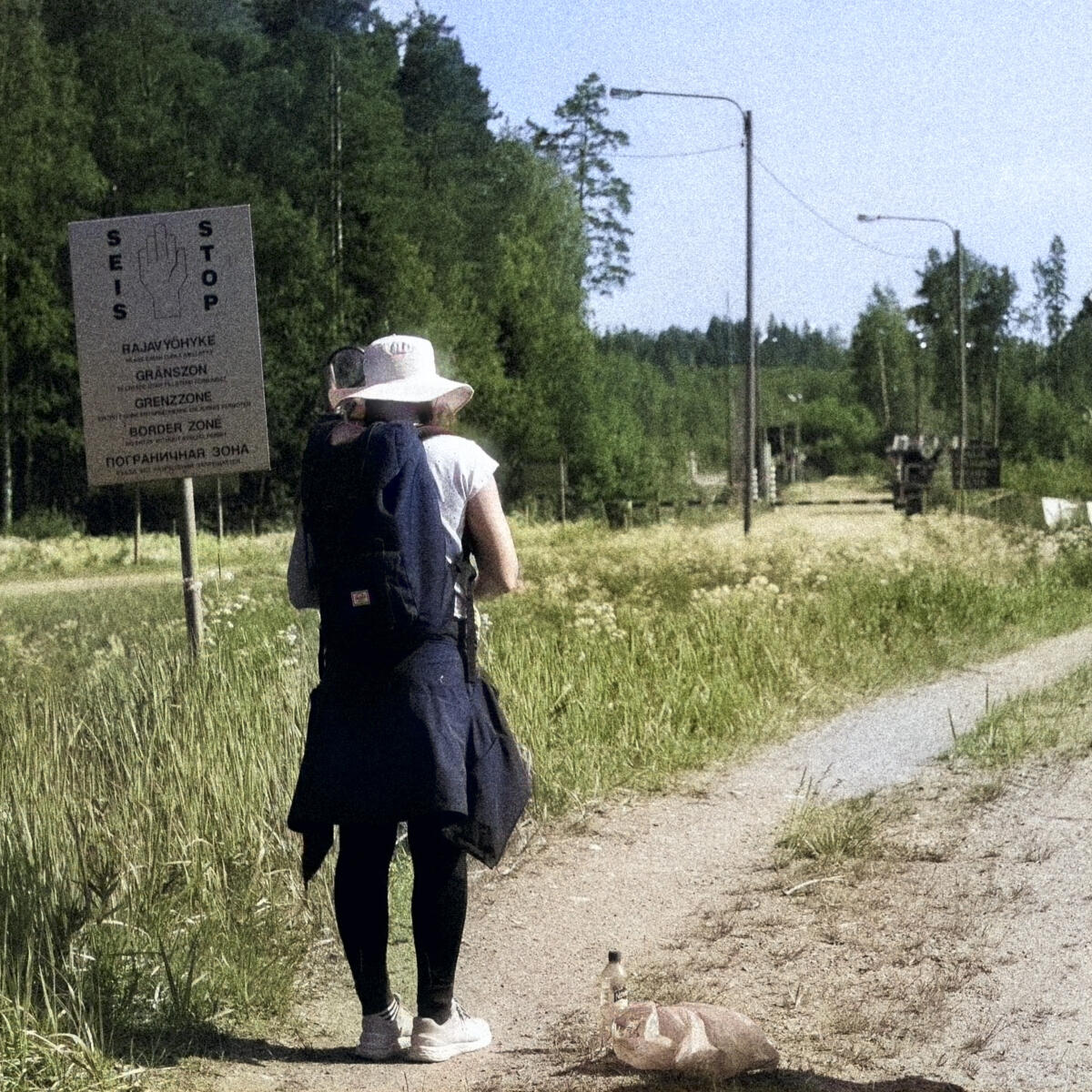 An image of a person standing on an old road with the sign of the Russian border before them.