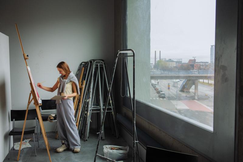 Kuvituskuva opiskelijasta Kuvataideakatemian tiloissa maalaamassa taulua.