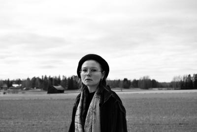 Mustavalkoinen kuva Anna Kirvesniemestä takanaan peltomaisema ja taivasta.