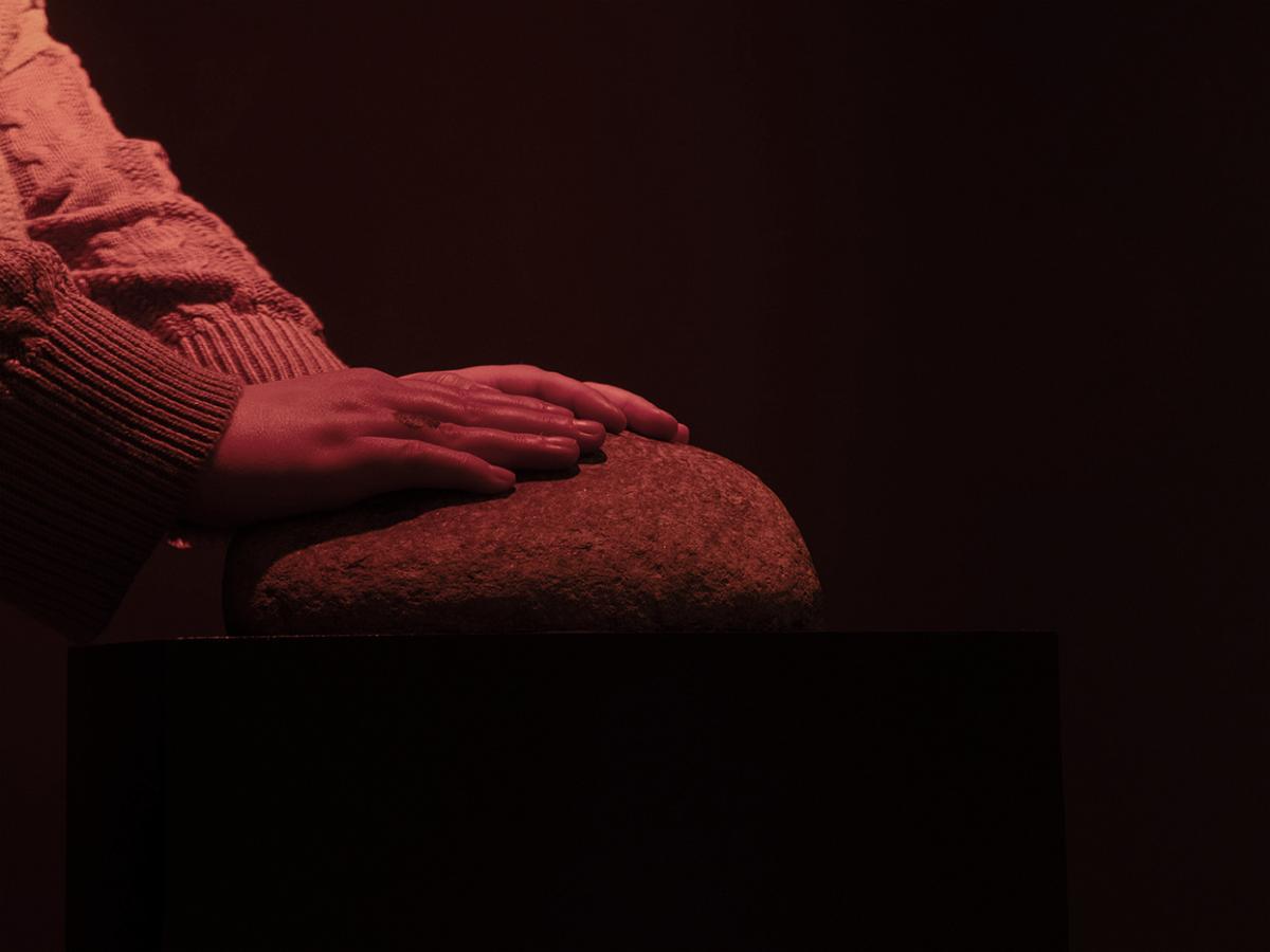 Pair of hands are resting on a smooth rock in red light. The background is dark.