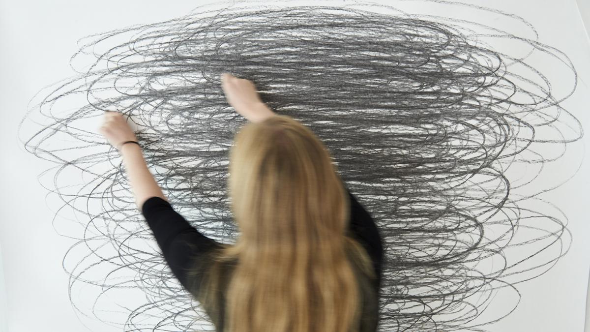 Naisoletettu piirtää isolle paperille mustaa pyörrettä.