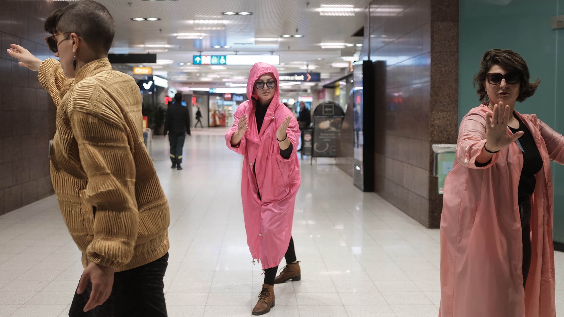 Three performers in a metro station posing, all wearing tinted eyewear, two facing the camera.