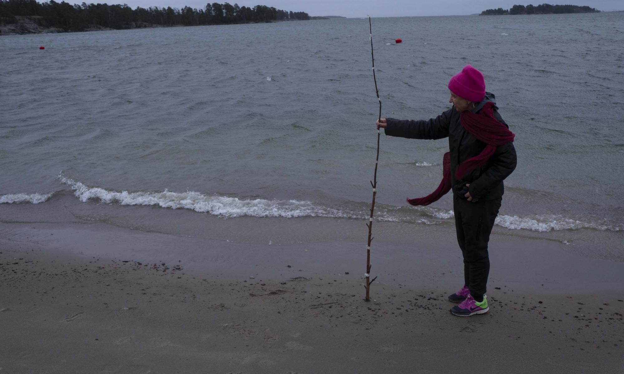 Marjatta Oja mittaa merenpinnan korkeutta rannalla.