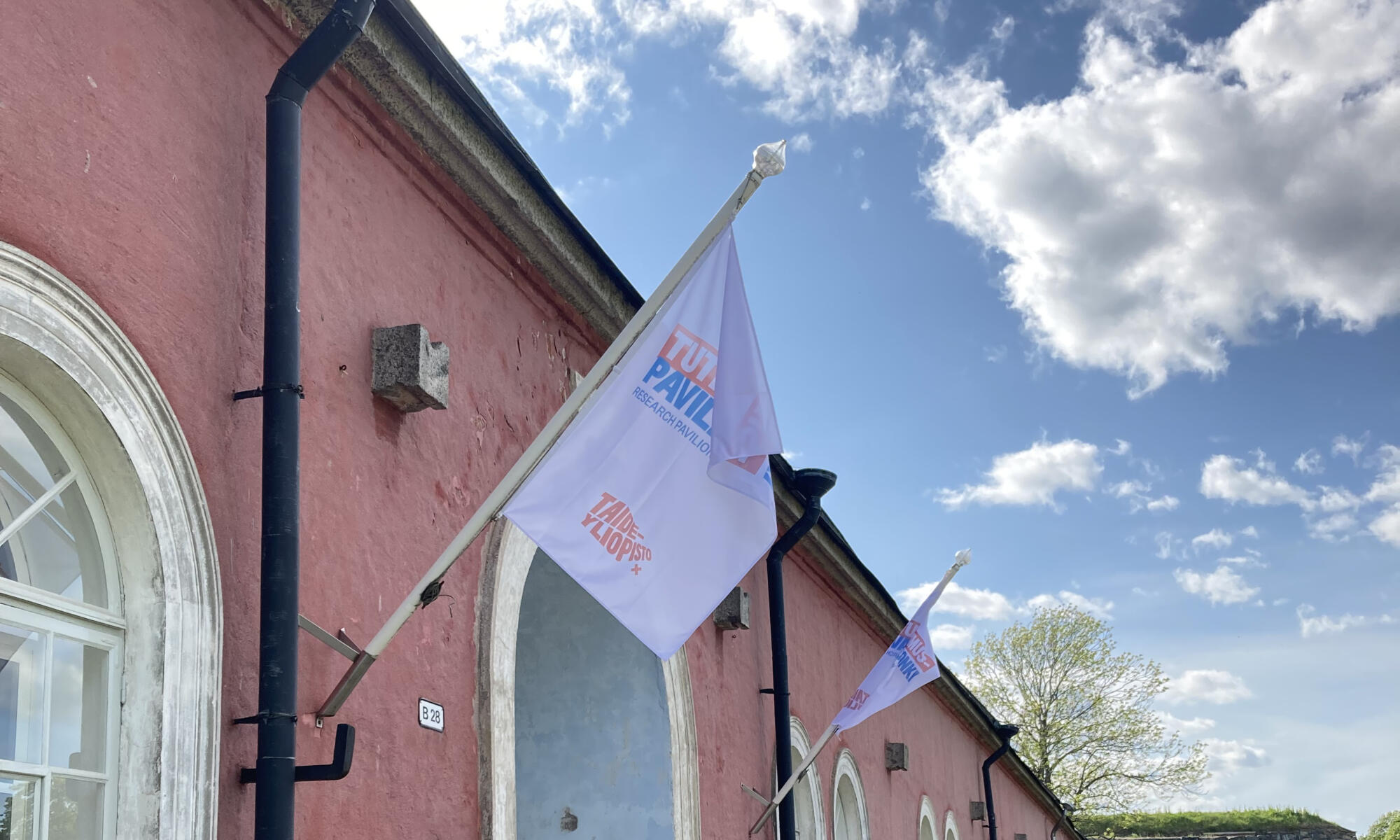 Research Pavilion flags, a pink stone wall building and blue sky.