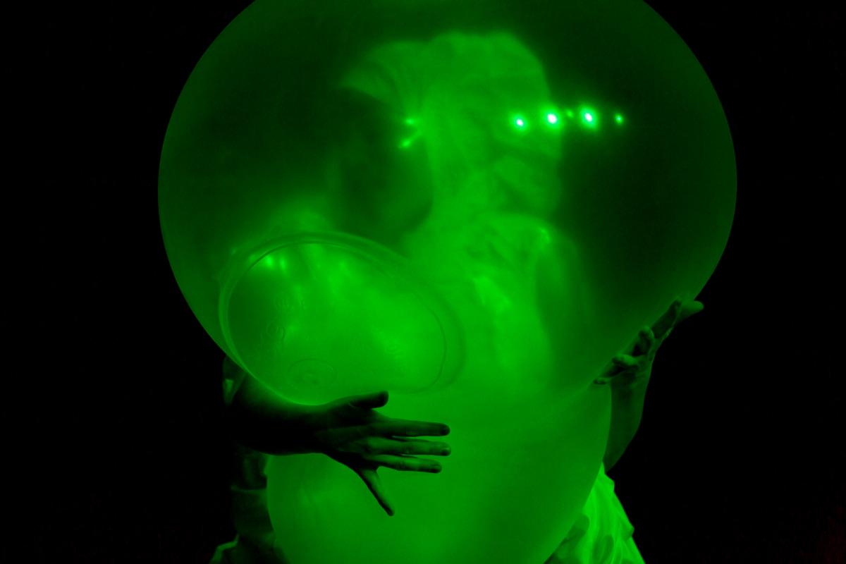 Green rubber balloon held in the arms of a performer.