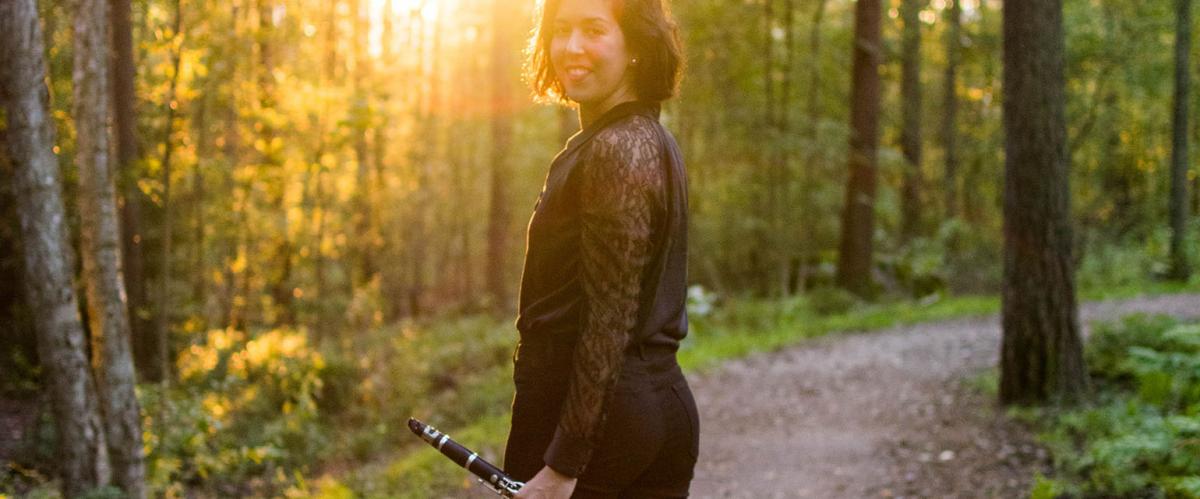 Lucy Abrams poseeraa klarinetin kanssa metsässä ilta-auringossa.