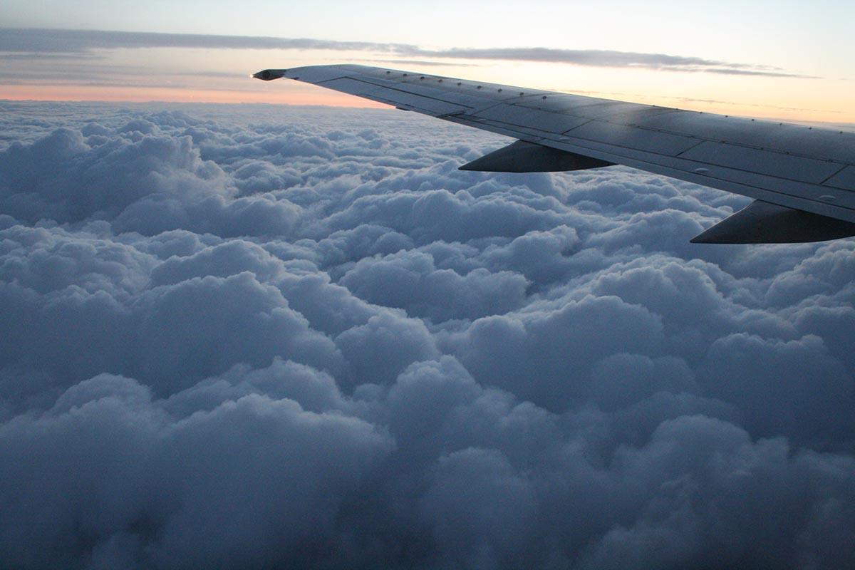 Lentokoneen siipi, taustalla pilviä ja auringonlasku