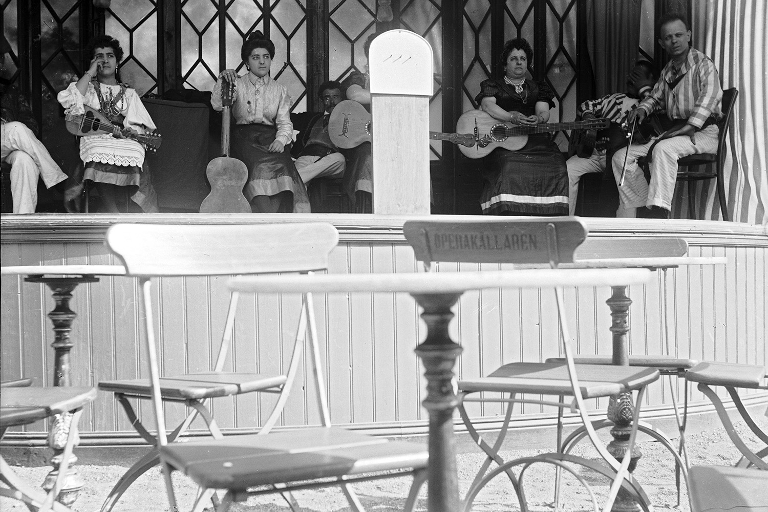 Historic black and white photo of women musicians performing on a stage outside in a park.