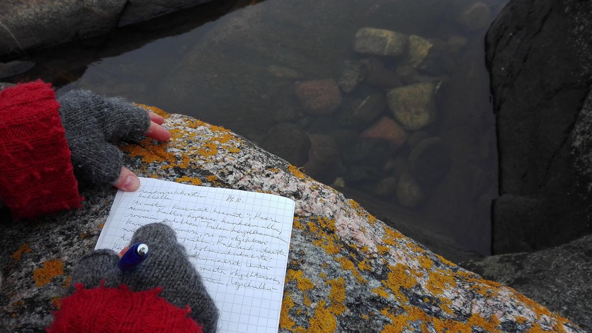 Ihminen kirjoittaa muistikirjaa kalliolla