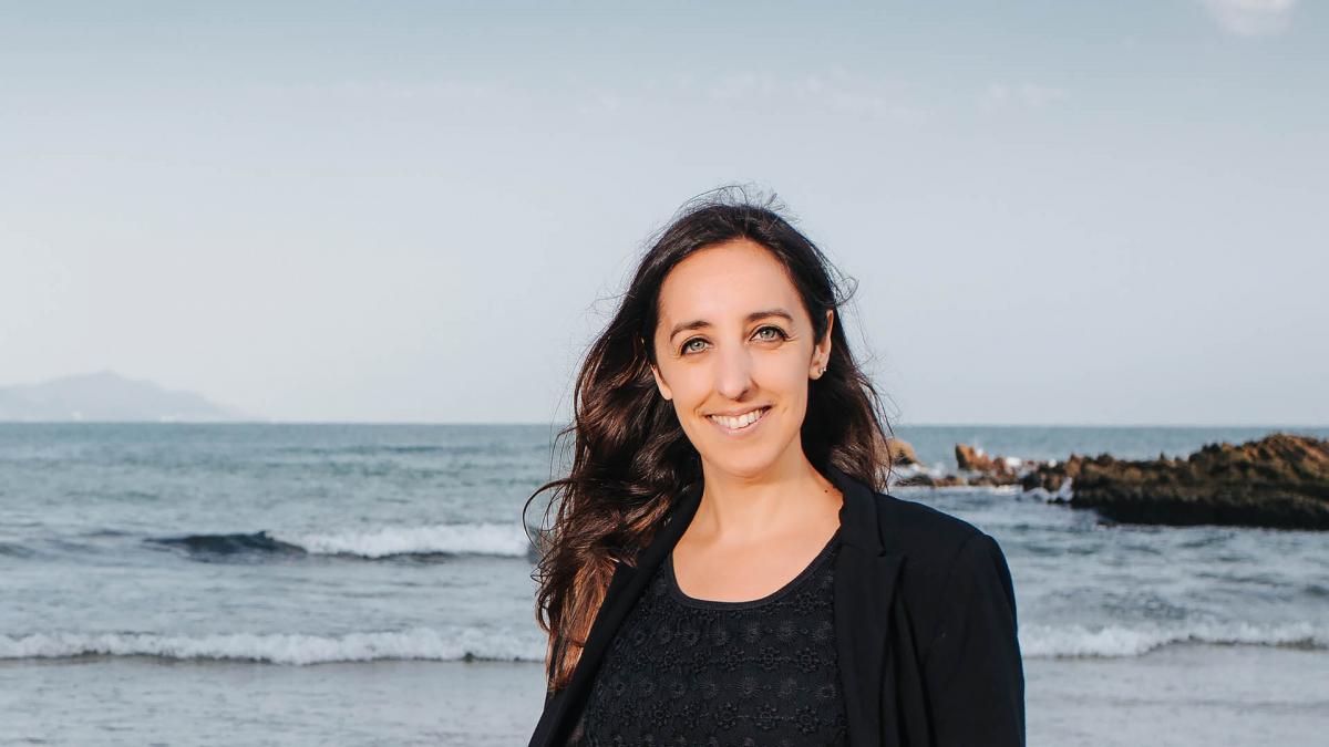 Naiara de la Puente Vadillo is standing in front of the sea, facing the camera with a smile.