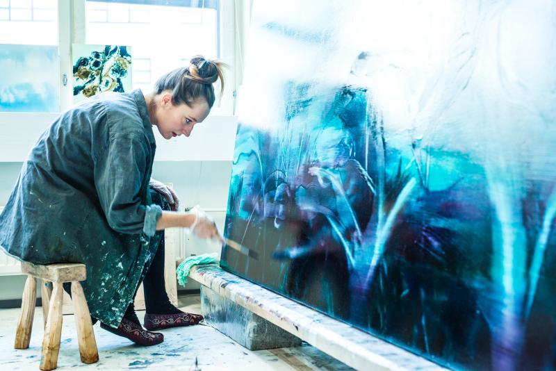 Opiskelija maalaa työhuoneella suurta sinistä maalausta
