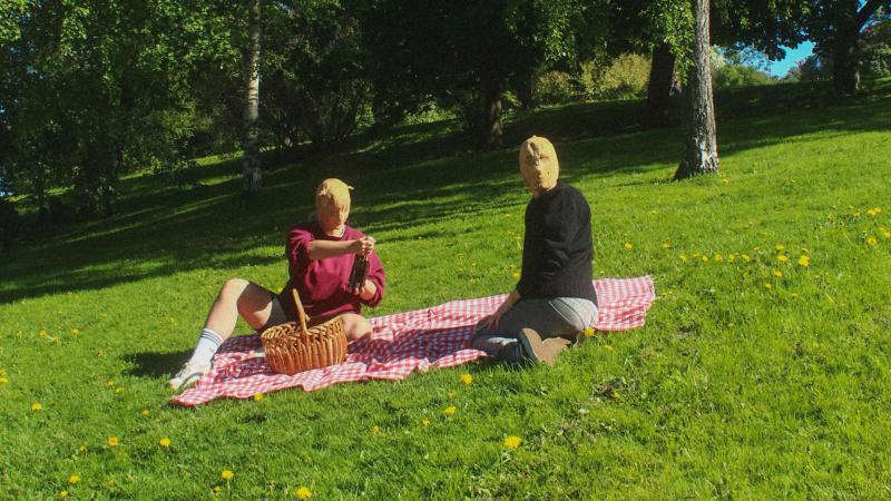 Two people sitting on a picnic blanket wearing masks.