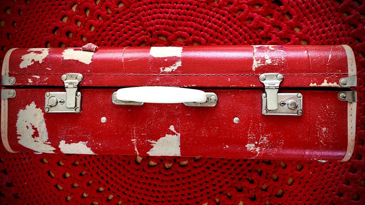 Kuvassa punainen matkalaukku, tausta punainen virkattu