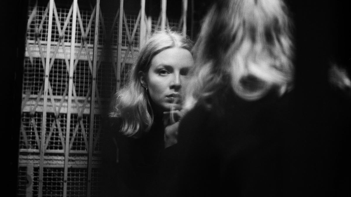 Lina Sandvik katsoo hissin peilin kautta suoraan kameraan.