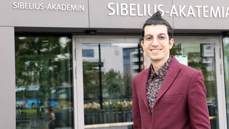 Ahoora Hosseini is smiling in fornt of the enteance of Sibelius-Academy