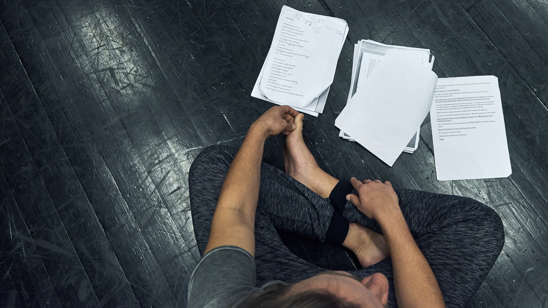 Person sitting cross-legged on black floor, papers with text placed on the floor.