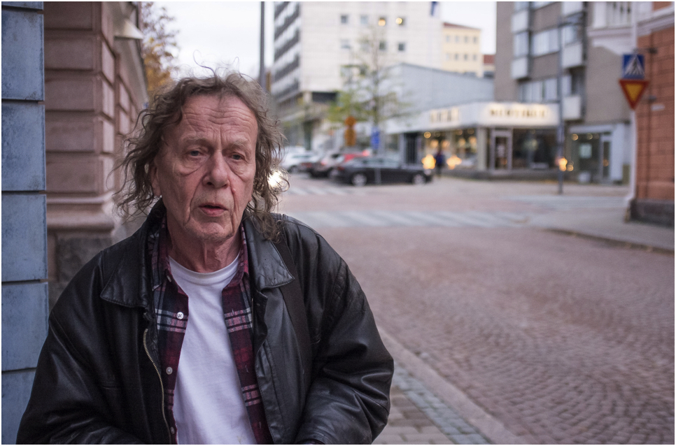 Jukka Ruohomäki stands on the corner of the street and looks past the camera.