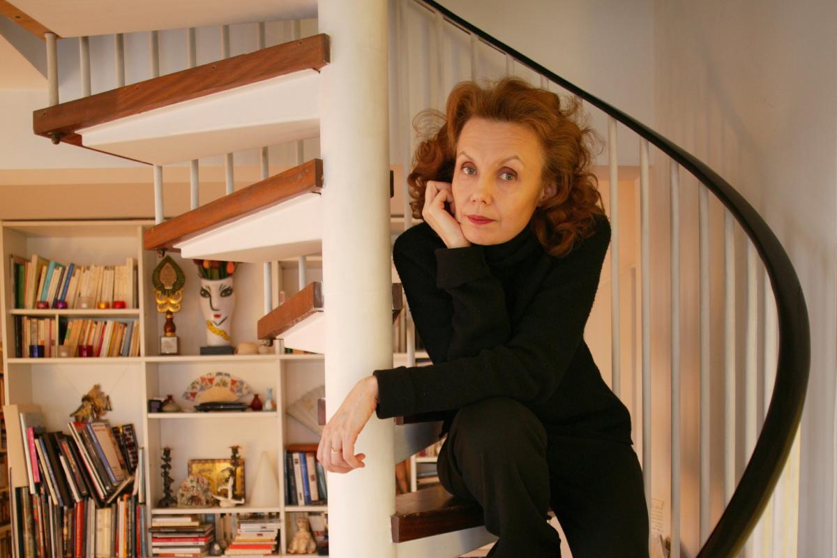 Säveltäjä Kaija Saariaho istuu portailla ja nojaa käteensä.