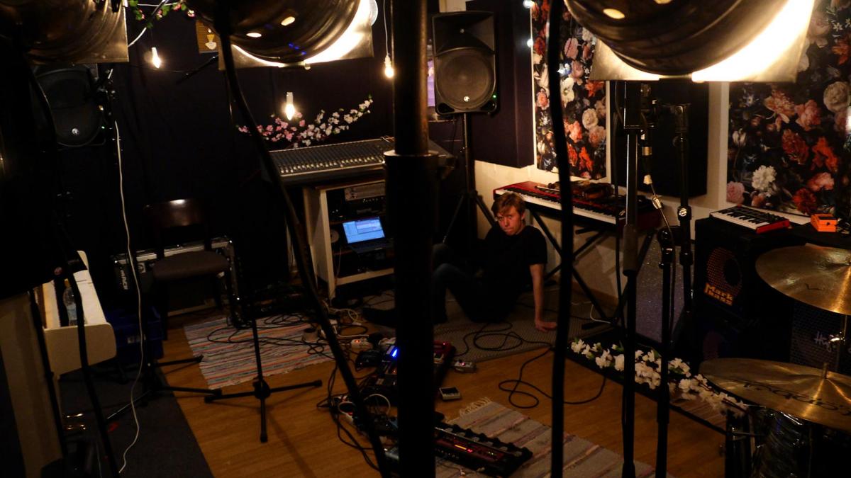 Elias Riipinen is sitting on the floor of a studio. The photo is taken behind some lights.