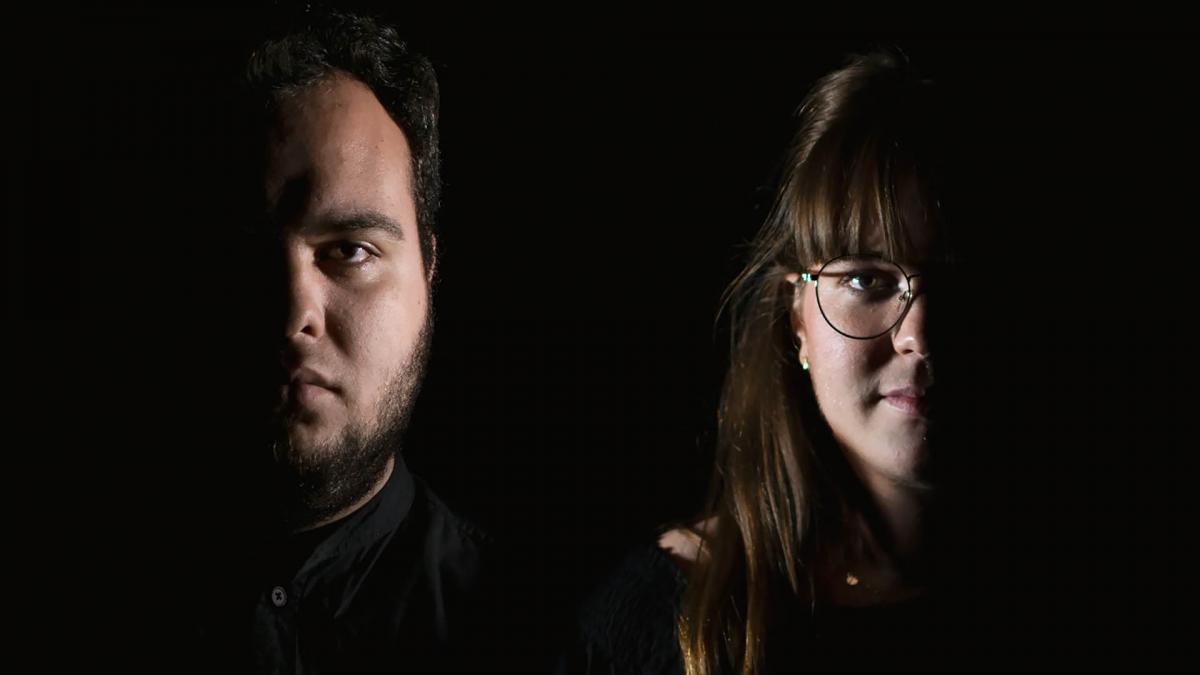 Claudia Reyes Segovia and Pau Fernández Benlloch are standing in a dark space. Only half of their both faces are showing.