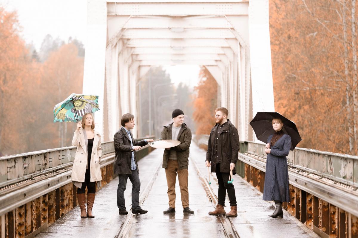 Echo Percussions -yhtye seisoo sillalla valokuvassa. Ulkona on sateinen keli, mutta kaikki ovat iloisia.