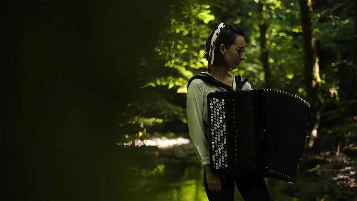 Woman is standing in the forest with accordion.