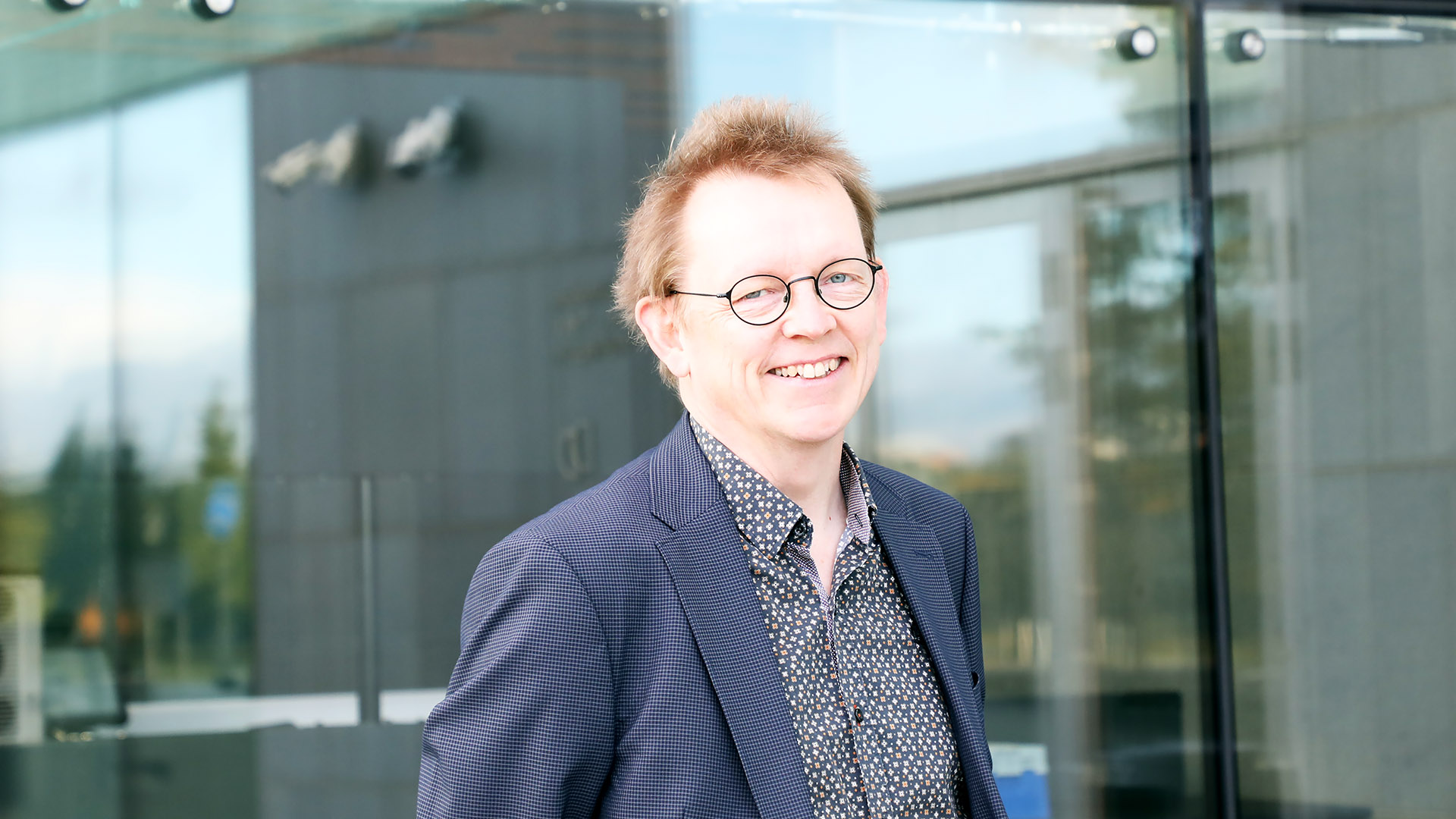 Juha Ojala stands before Music Centre's glass wall and smiles for the camera.