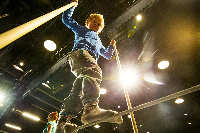 A child is walking on the rope and looks downwards at the camera.