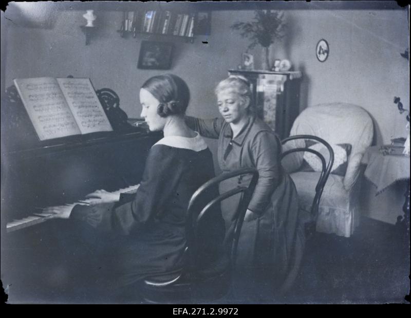 Kaksi naista istuu pianon äärellä mustavalkoisessa kuvassa. Nuorempi soittaa, vanhempi kuuntelee.