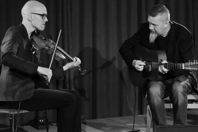 Esko Järvelä soittaa viulua istuen. Hänen vieressään Roger Tallroth soittaa kitaraa tuolilla istuen.