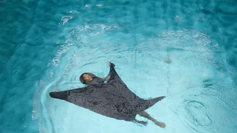 A person is floating in the water in a dark dress that floats around them.