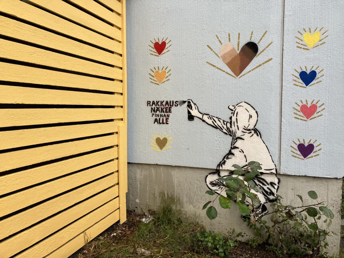 Seinämaalaus spray-maalaavasta hupparihahmosta, joka on kirjoittanut seinään "Rakkaus näkee pinnan alle".