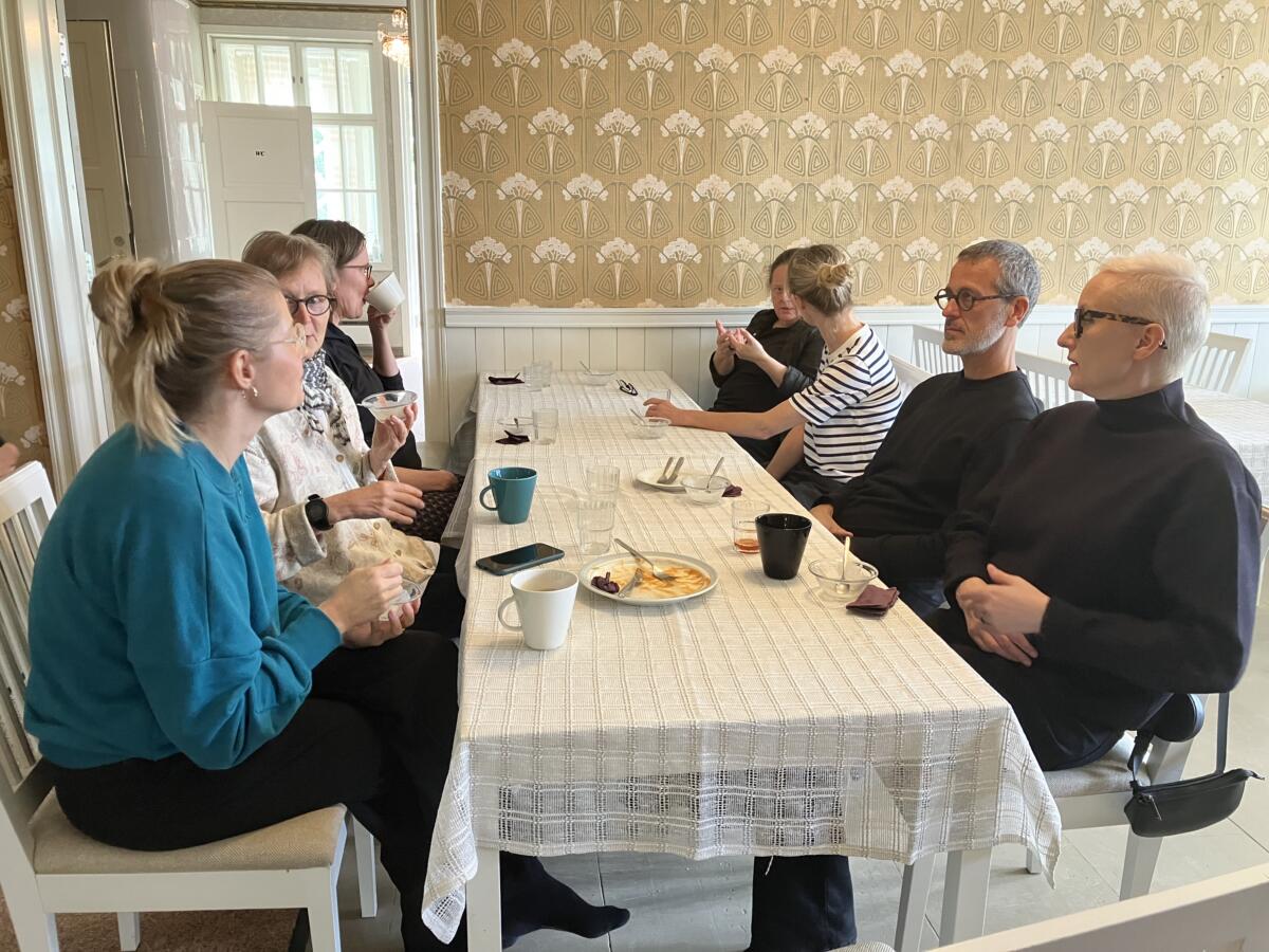 Researchers sitting around a table with a white table cloth and coffee cups in a light colored room.