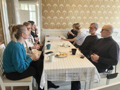 Researchers sitting around a table with a white table cloth and coffee cups in a light colored room.