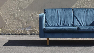 Sininen sohva kadulla, taustalla harmaa betoniseinä.