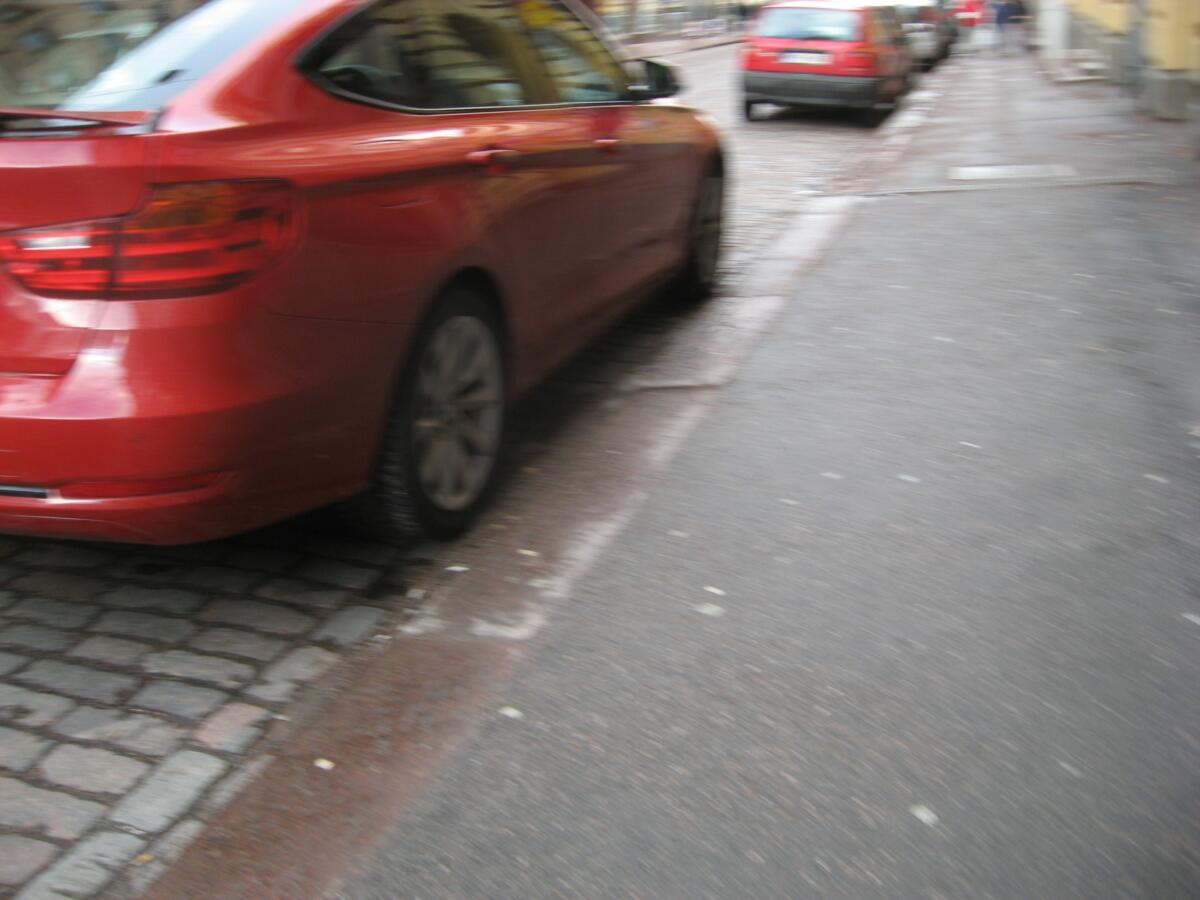 Kuva punaisesta autosta pysäköitynä jalkakäytävän viereen.
