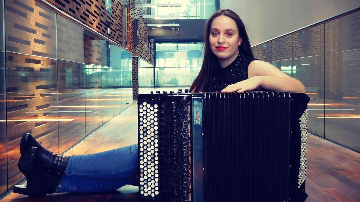 Manca is sitting on a Music centre hall with her accordion. She is smiling on the camera.