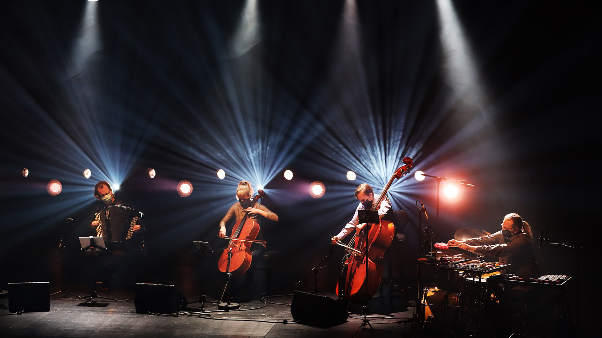 Drummer, two cellists and accordionist playing on a stage.